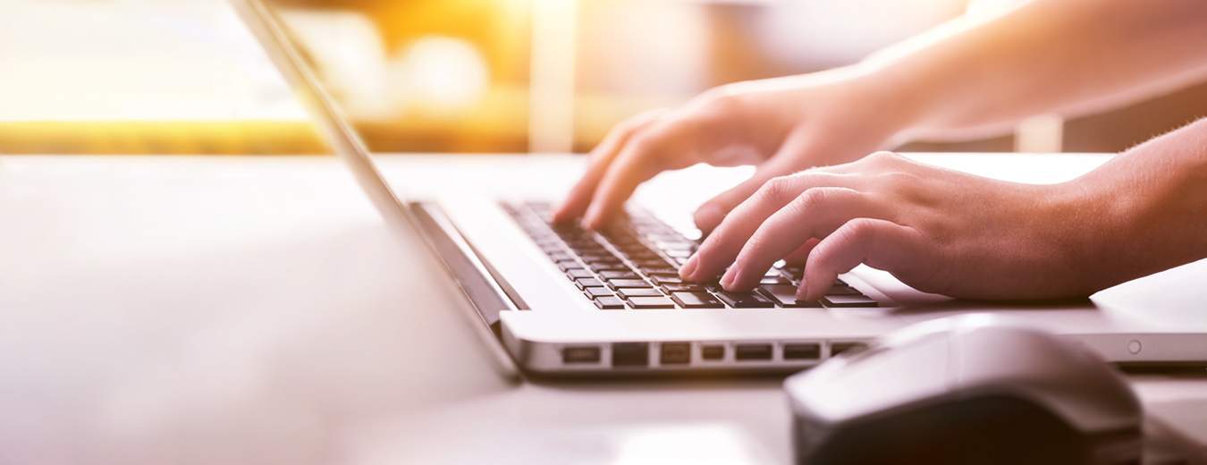 Hands typing on a laptop keyboard, with a mouse nearby and a warm, soft light in the background