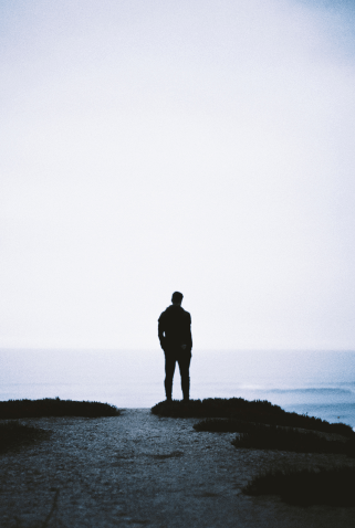 A solitary figure standing on a cliff overlooking the ocean, silhouetted against a pale sky