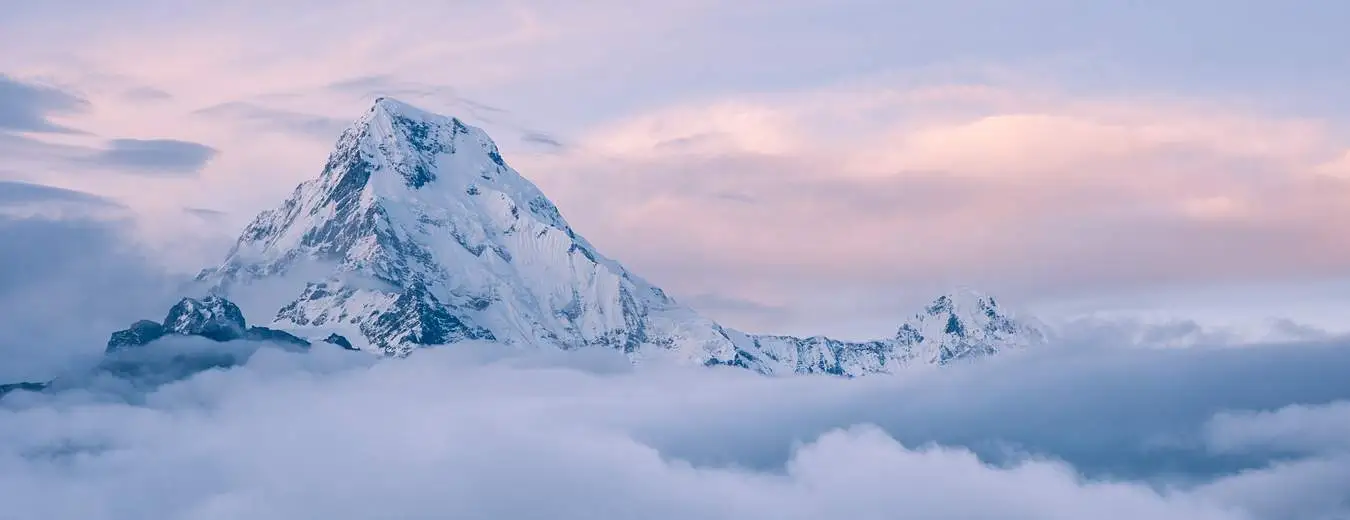 Snow-capped mountain peak emerging above the clouds with a soft pink and blue sky in the background