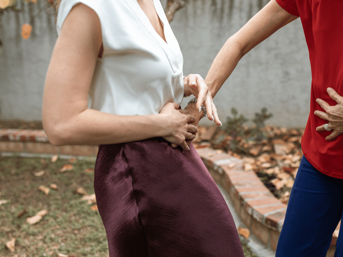 A close-up of two women in an outdoor setting, with one woman placing her hands on the other's abdomen