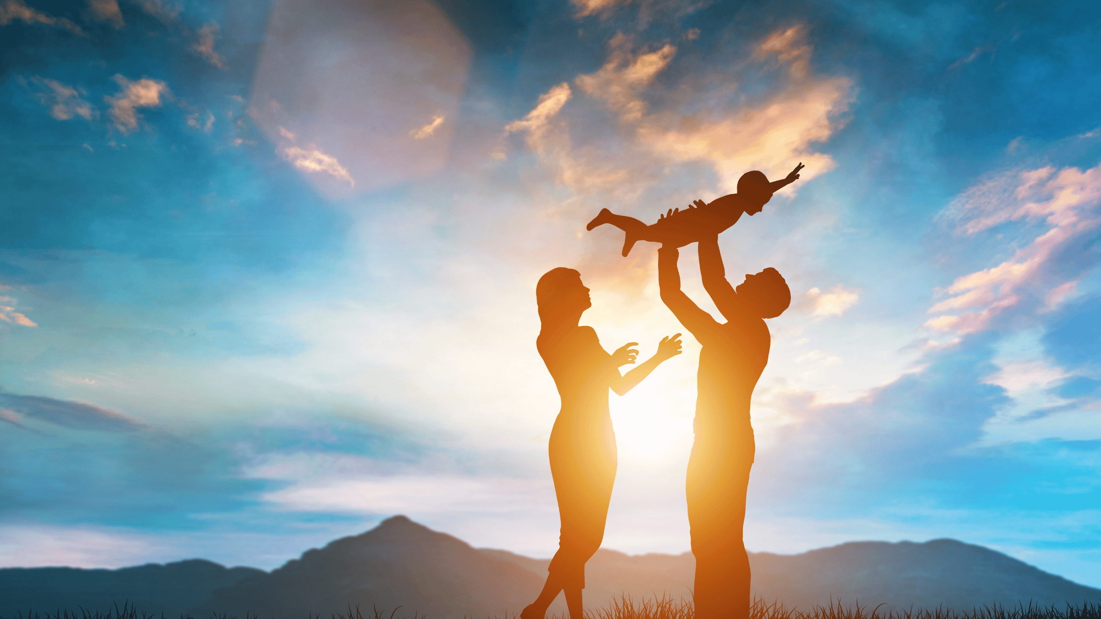 Silhouette of a family at sunset, with a man lifting a child in the air and a woman reaching toward them, set against a vibrant sky with mountains in the background