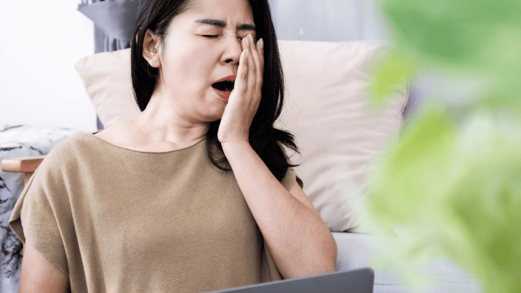 A woman yawning while sitting on a couch, symbolizing the persistent tiredness caused by depression fatigue, and the cycle of exhaustion and low energy. Why Does Depression Make You Tired?