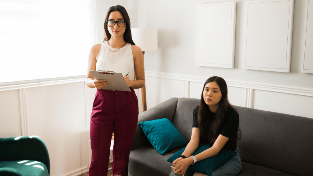 A therapist standing next to a seated patient, symbolizing the process of seeking help for depression, including therapy to manage fatigue and mental health. Why Does Depression Make You Tired?