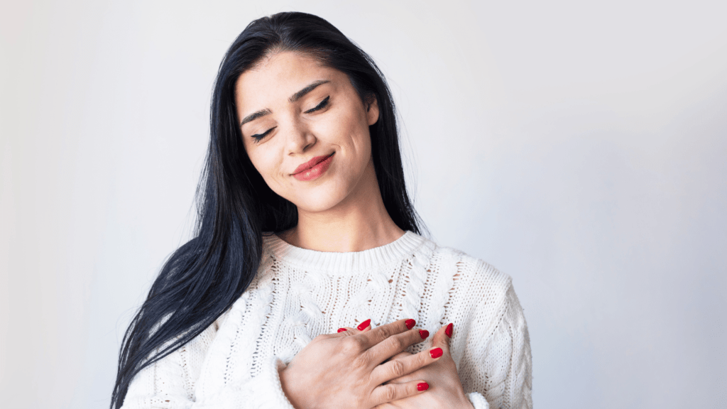 A woman gently holding her chest, representing self-compassion, positive self-image, and mental health improvement through self-acceptance practices.