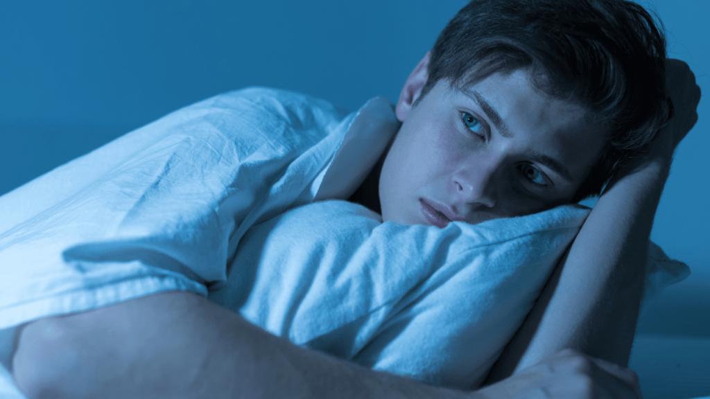 Young man lying awake in bed, looking pensive and staring off into the distance.