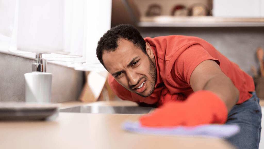 Man intensely scrubbing a kitchen counter with a focused expression, wearing red gloves.