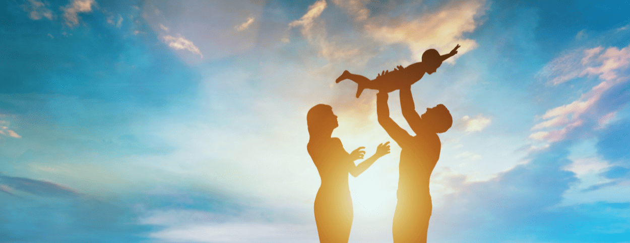 Silhouetted family at sunset, with a father lifting a child into the air and a mother reaching out joyfully, symbolizing the connection and support offered through coaching for donor conception parents.
