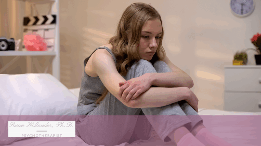 Teen girl sitting on bed with knees pulled to chest, appearing withdrawn and anxious, reflecting symptoms of Generalized Anxiety Disorder.