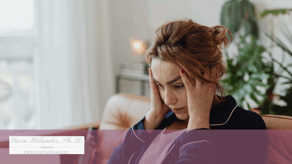 A woman sits on a couch holding her head in distress, appearing overwhelmed with emotion in a softly lit, therapeutic setting.