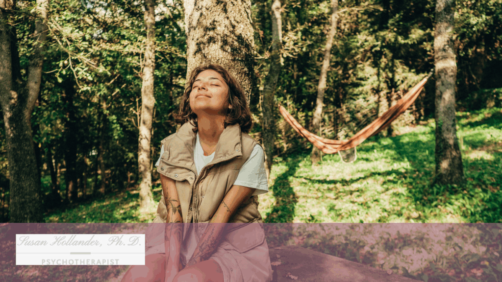 Smiling woman sitting peacefully in a sunlit forest, eyes closed and face lifted, representing calm and emotional restoration.